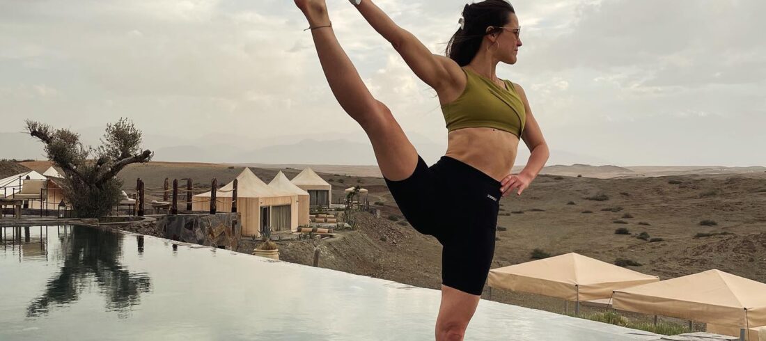 A woman in a moment of peaceful balance, performing a yoga pose by an infinity pool, embodying wellness with the vast Agafay Desert stretching into the horizon.